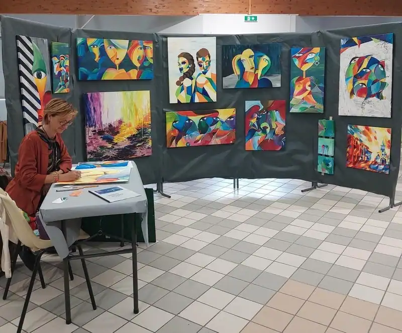 Christel à son stand d'exposition, devant une dizaine de ses tableaux colorés